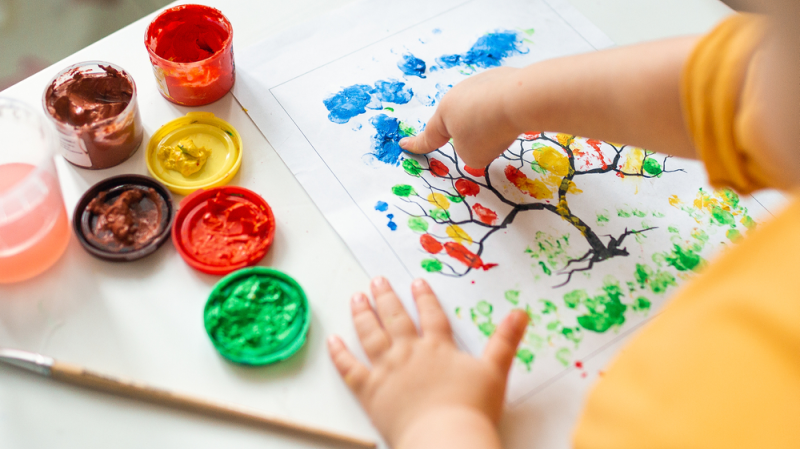 Niño pinta árbol de colores con el dedo
