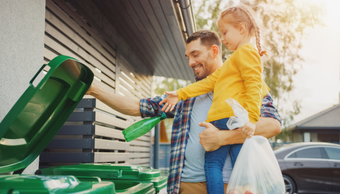 Papá con niña pequeña deposita basura en bote