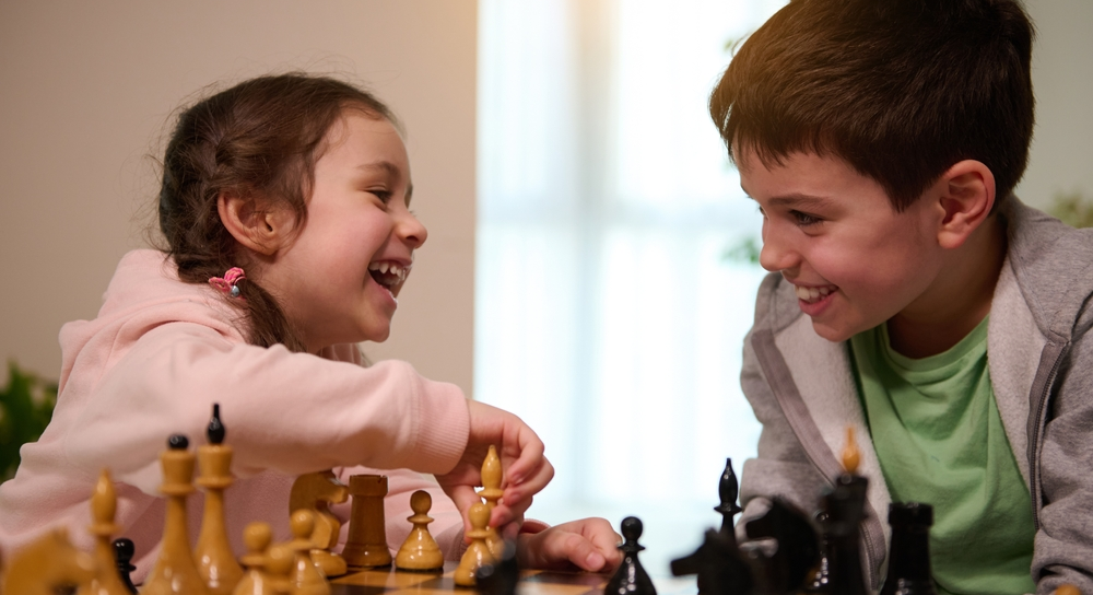 Niño y niña juegan ajedrez y se divierten