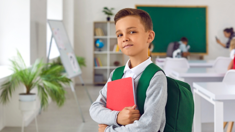 Niño inteligente con mochila y libro en aula